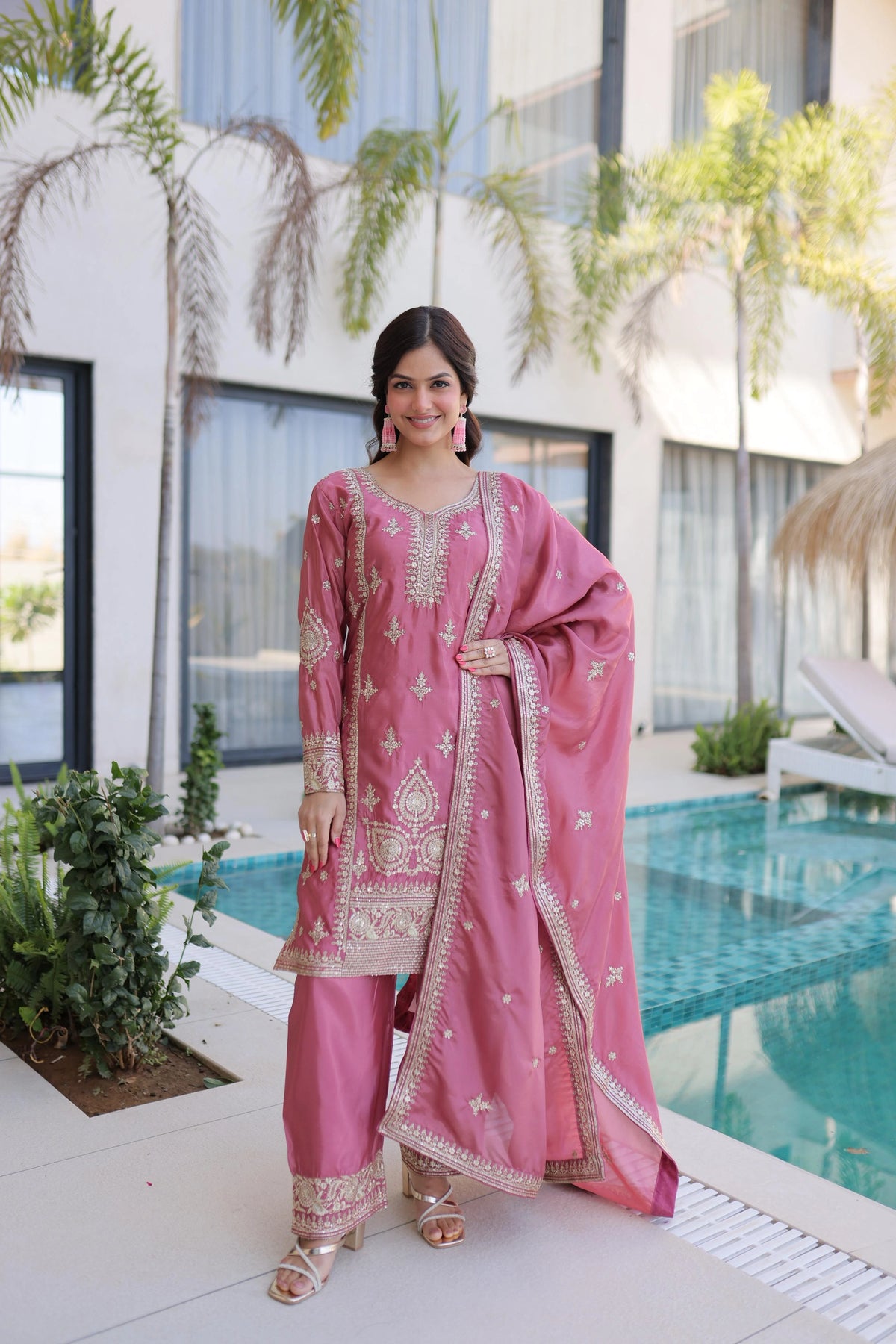 Woman in a pink traditional outfit standing by a pool with a modern building in the background