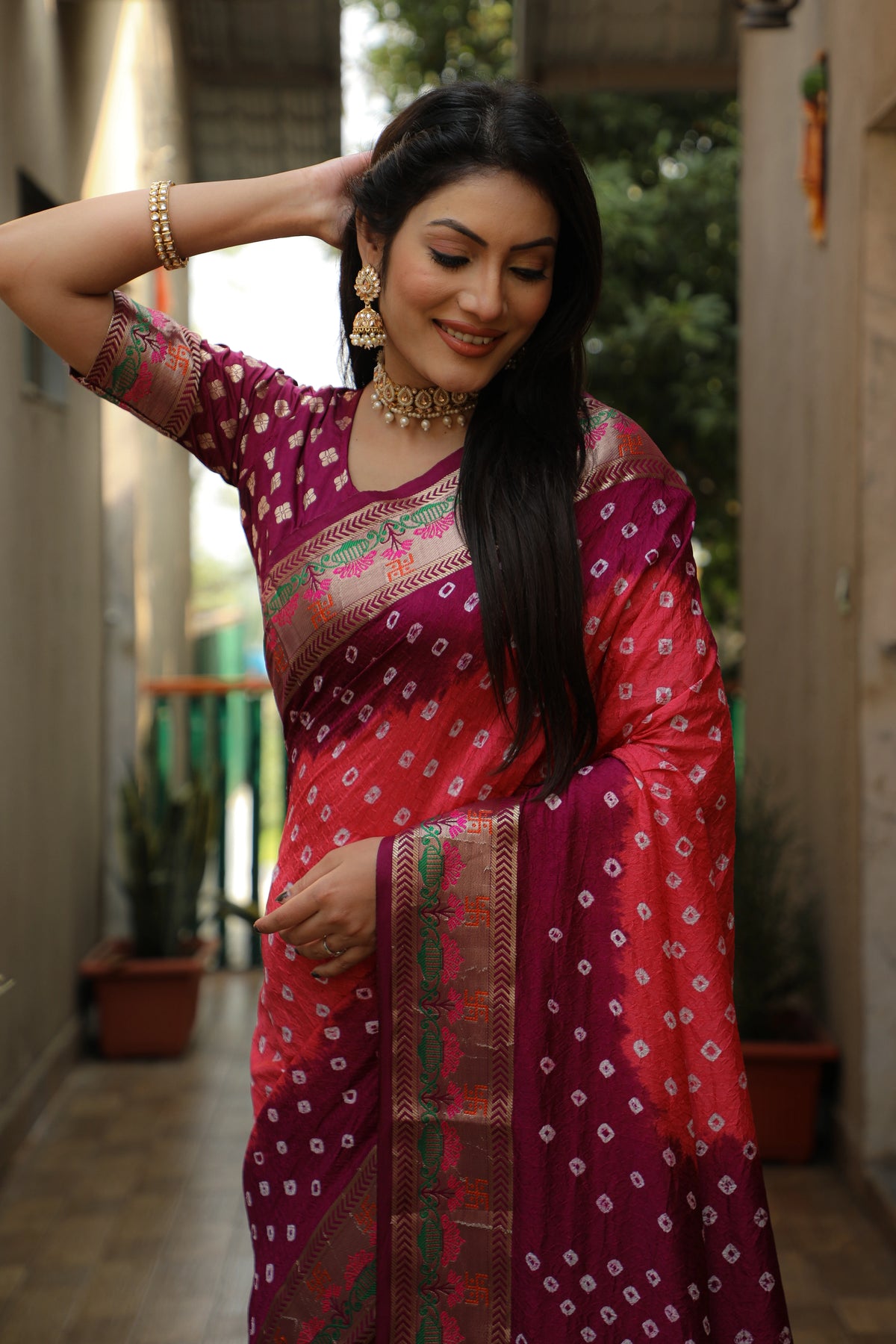 Woman in a traditional pink saree with a patterned blouse, standing outdoors.