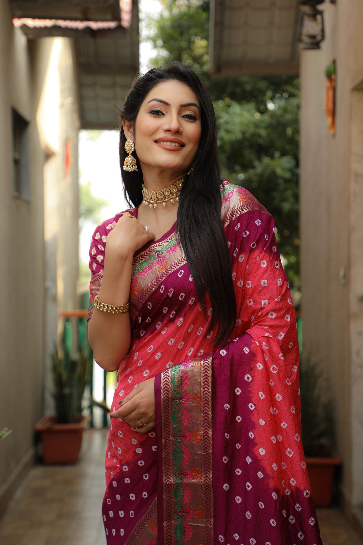 Woman in a traditional pink saree with a pattern, standing outdoors.