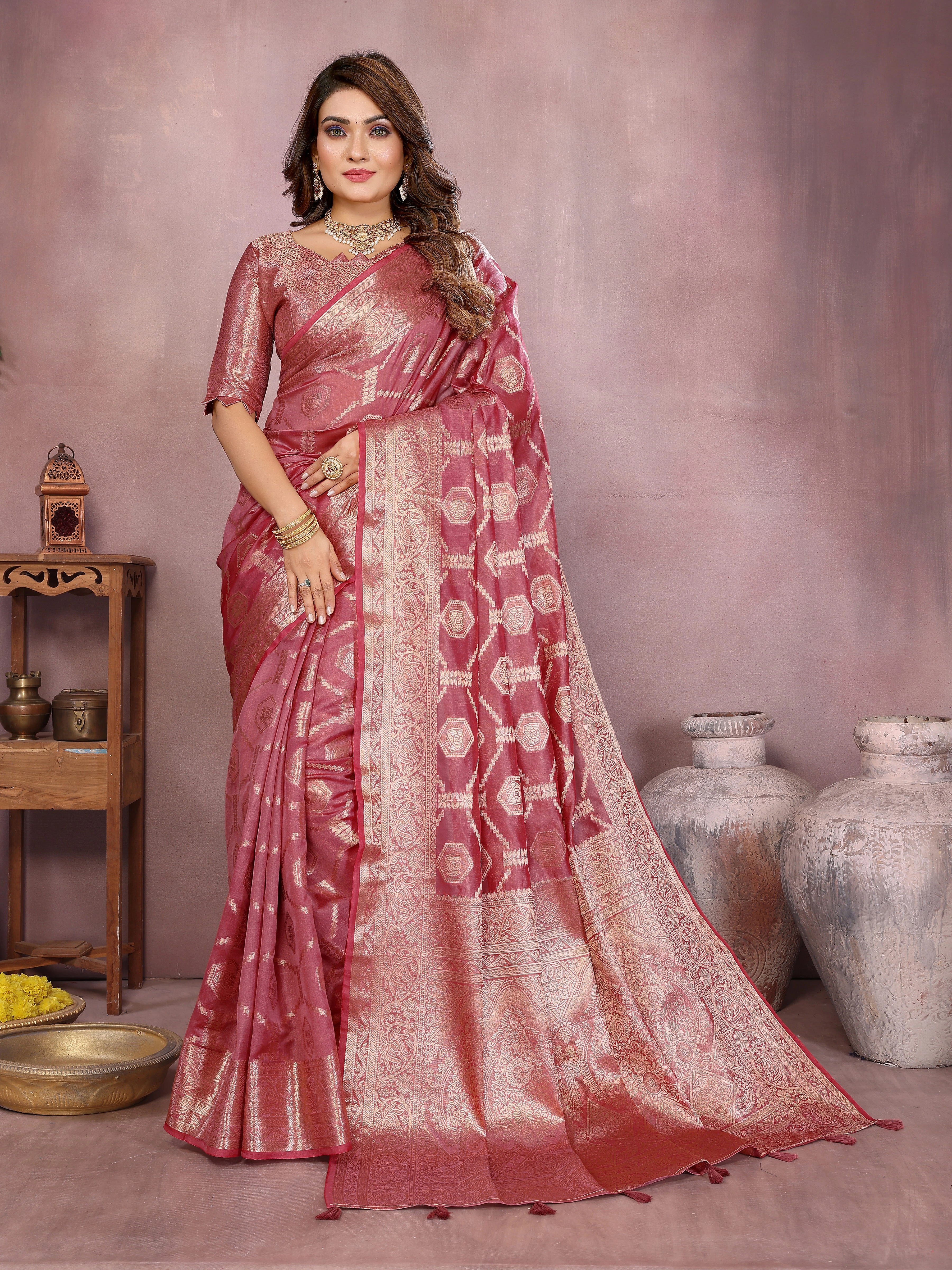 Woman wearing a pink saree with a subtle pattern in an indoor setting.