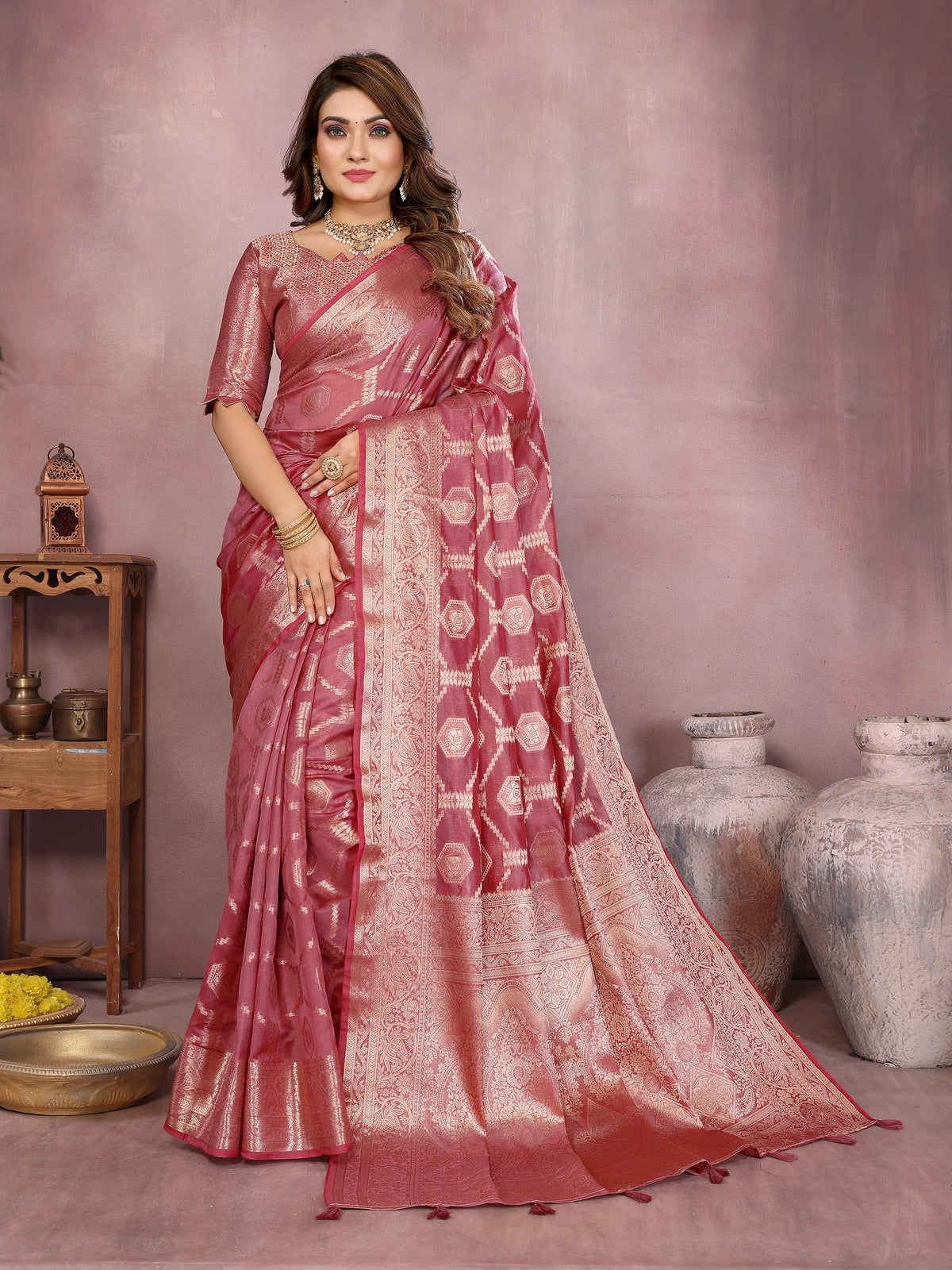 Woman wearing a pink saree with a subtle pattern in an indoor setting.