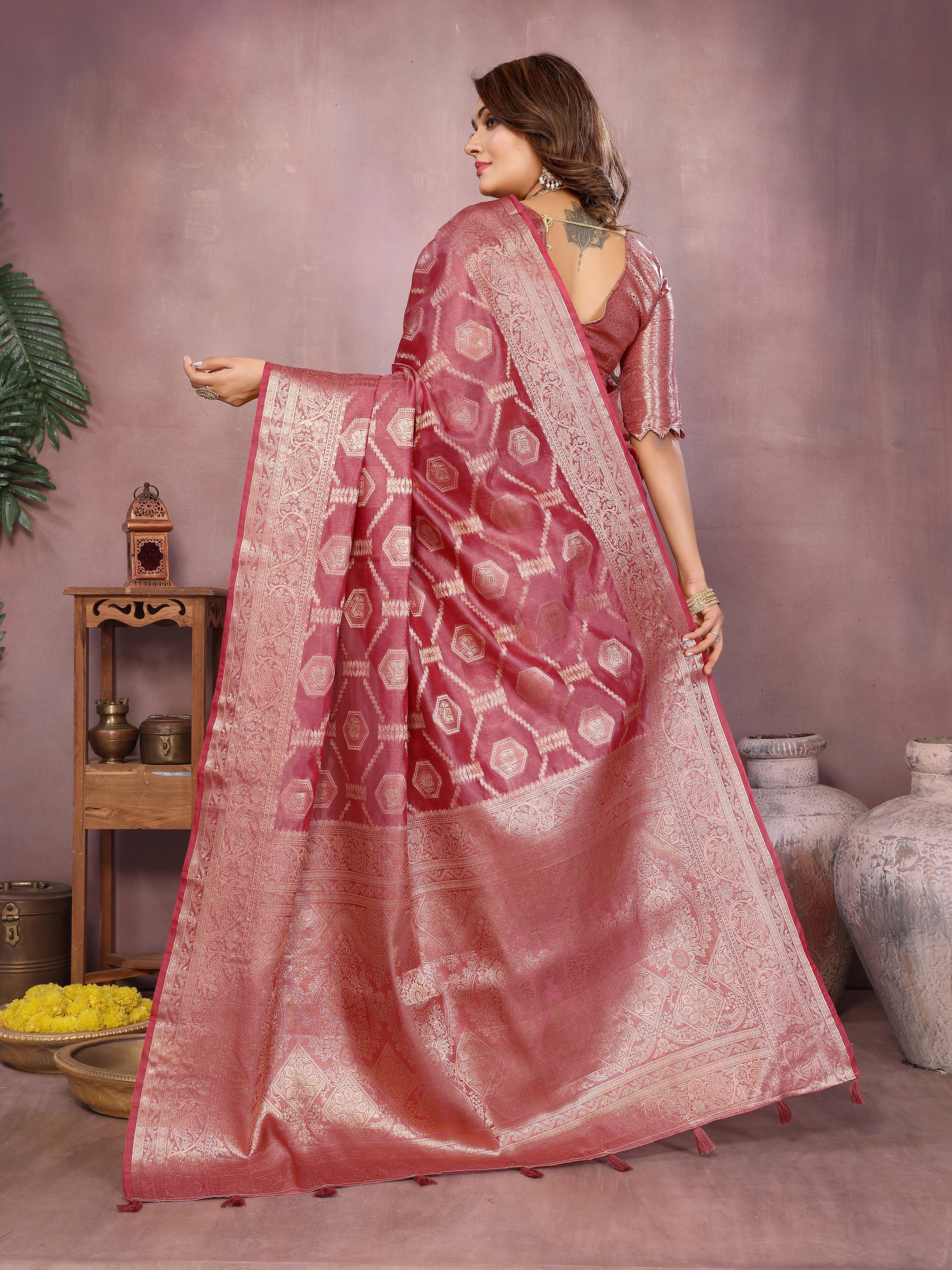 Woman wearing a pink saree with a patterned border, standing against a neutral background.