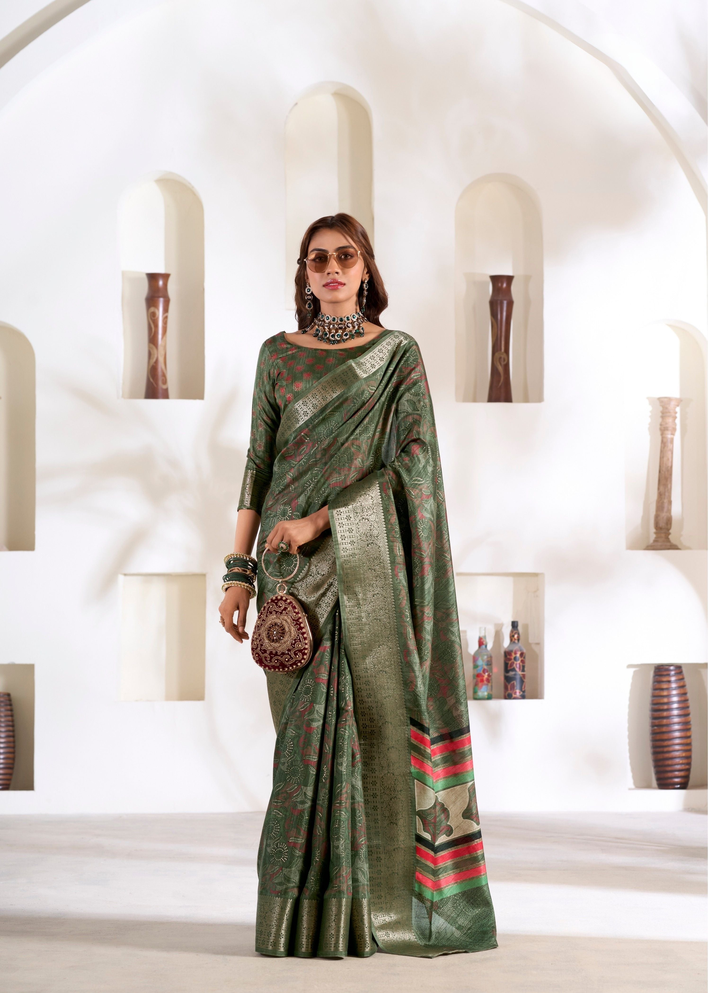 Woman in a green saree with red patterns standing in a white interior setting.