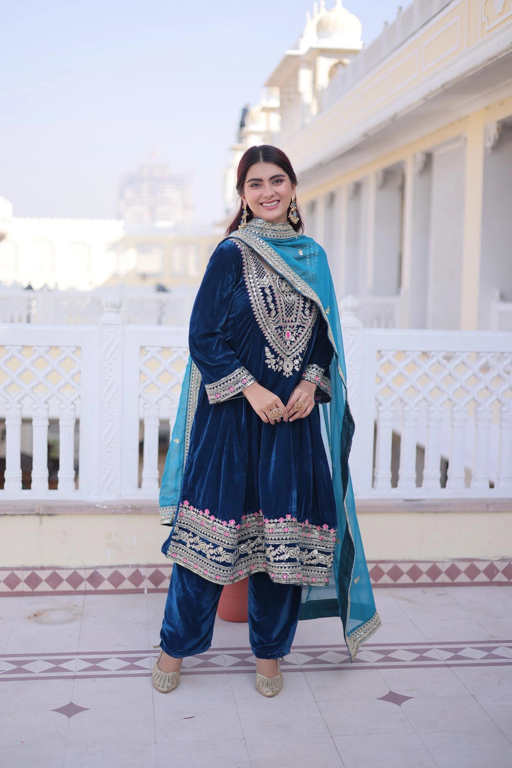 Woman in traditional blue and green outfit standing in front of a white building.