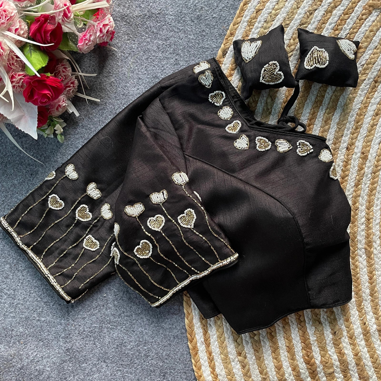 Black saree with heart-shaped embroidery on a textured surface with flowers.
