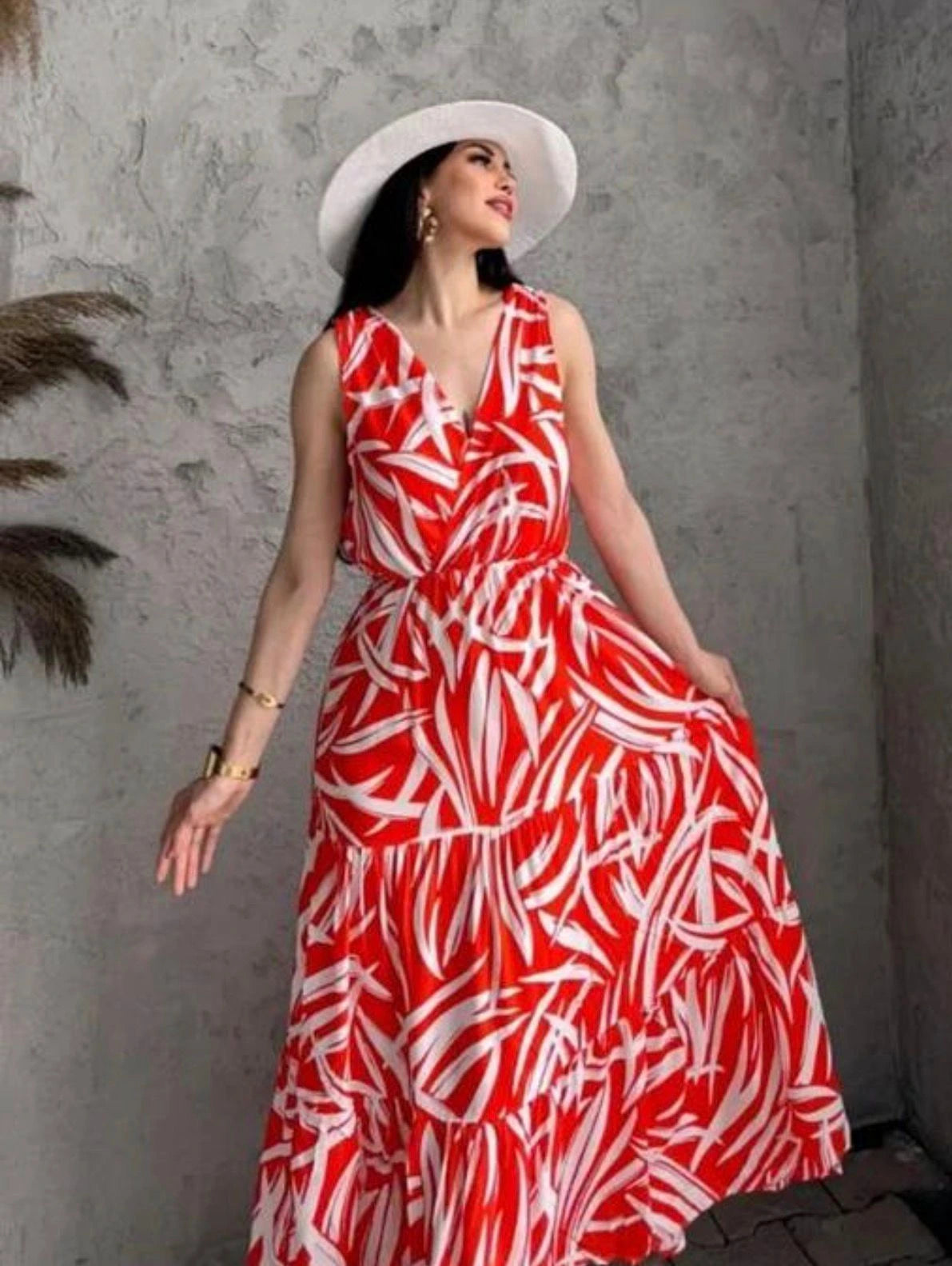 Woman wearing a red and white patterned dress with a white hat against a gray wall.