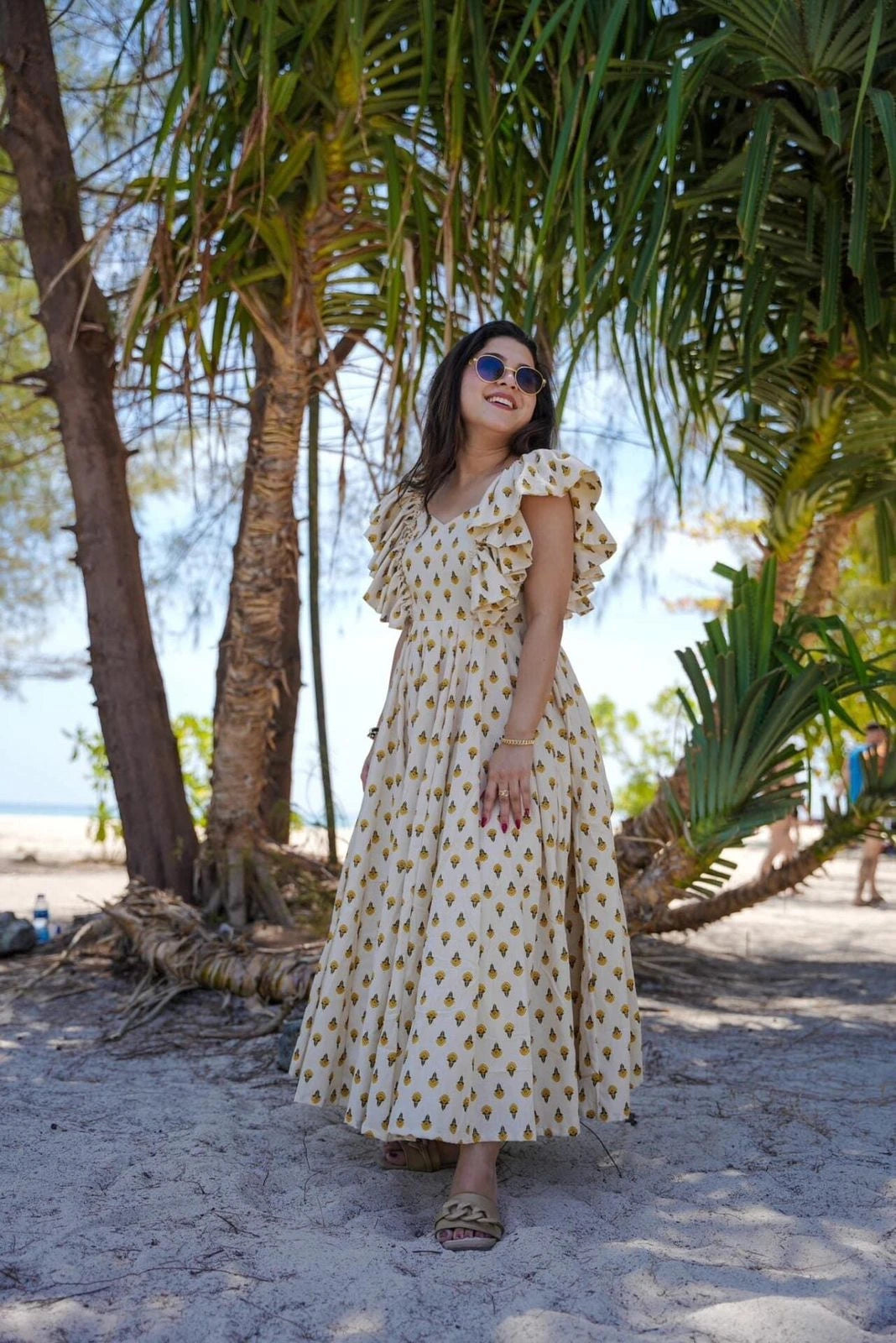 Woman in a polka dot dress standing under palm trees on a beach.