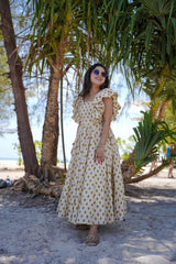 Woman in a polka dot dress standing under palm trees on a beach.