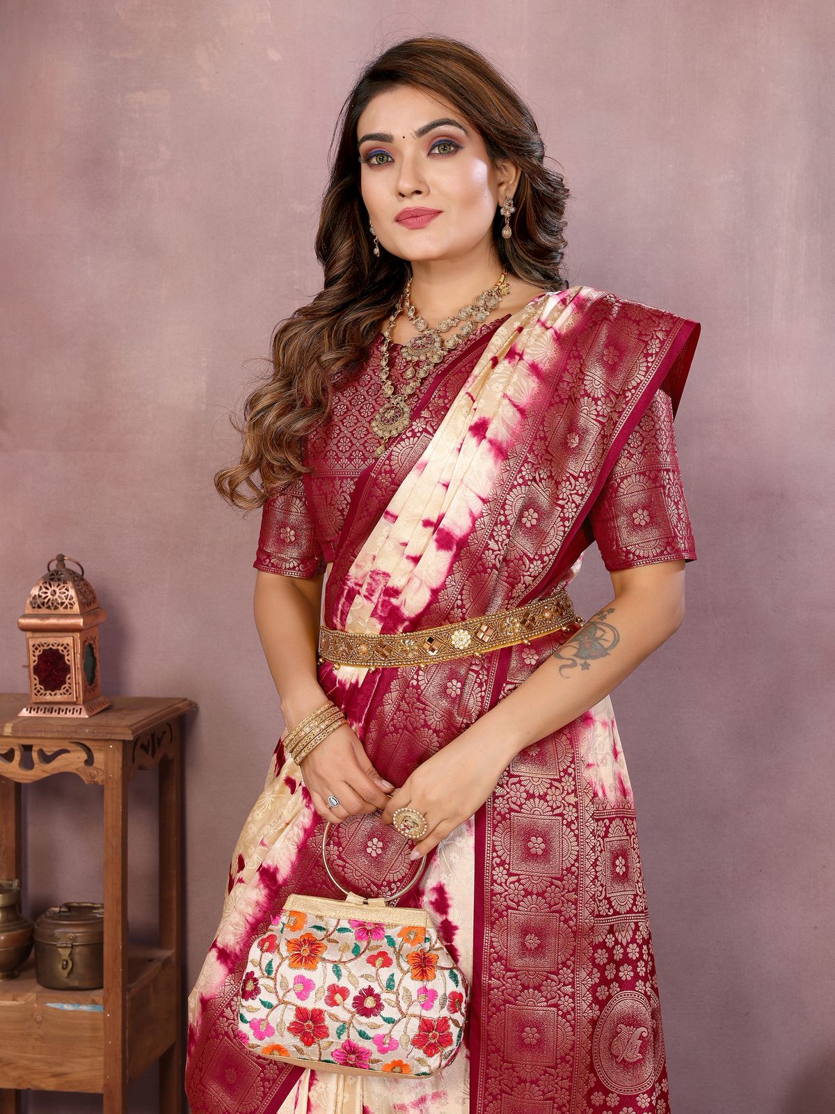 Woman wearing a red and white saree with a floral handbag against a plain background