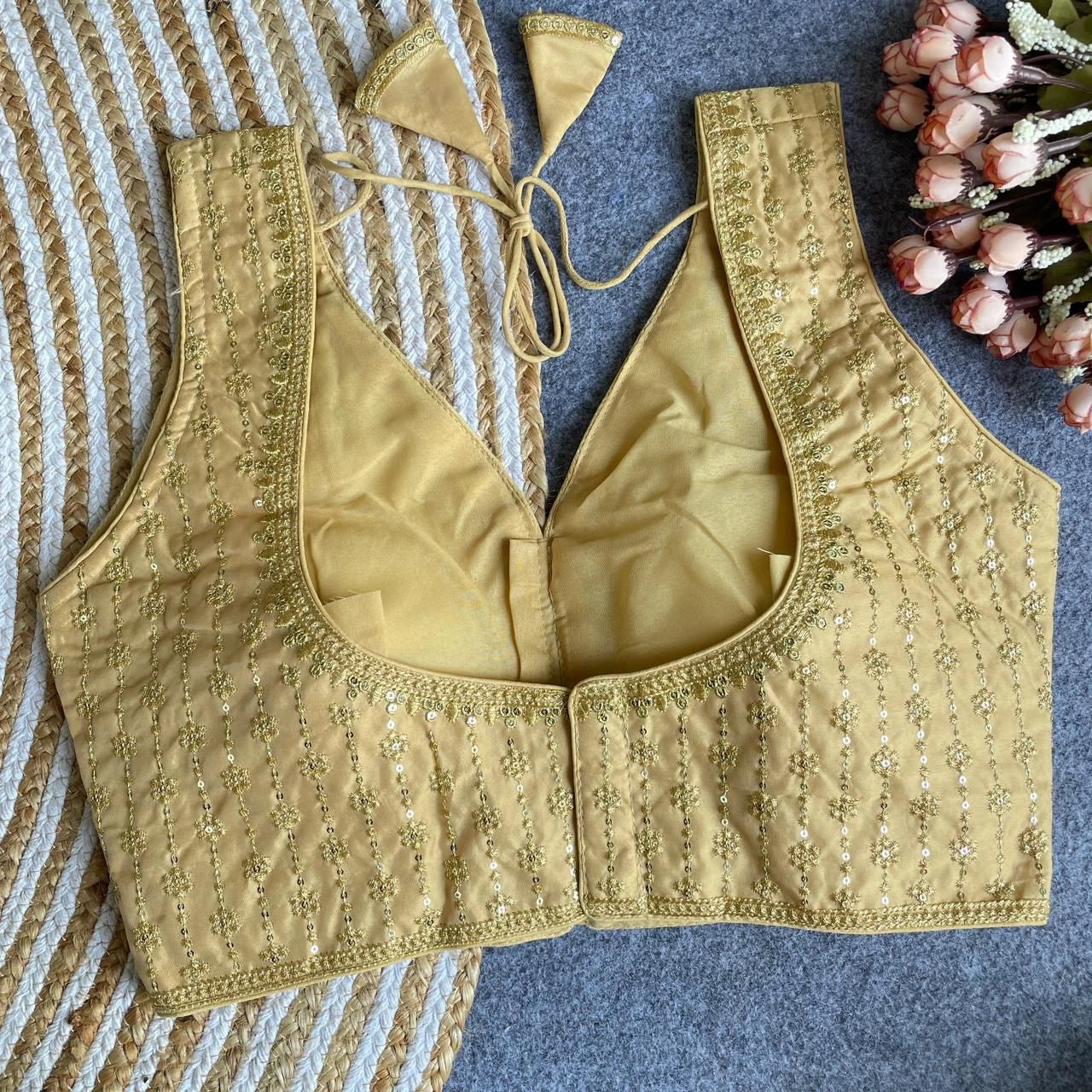 Gold embroidered blouse on a textured surface with flowers in the corner