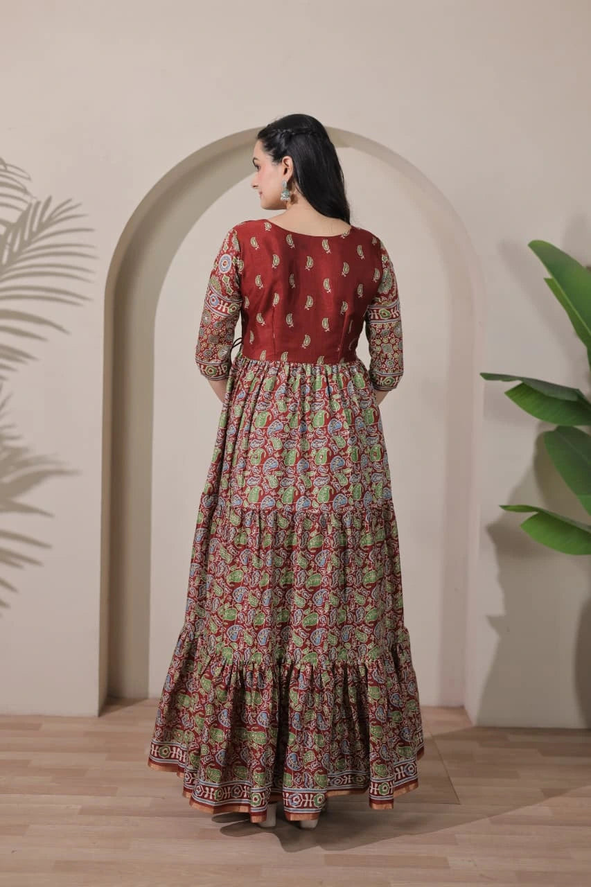 Woman wearing a red and floral patterned dress standing in front of an archway with plants.