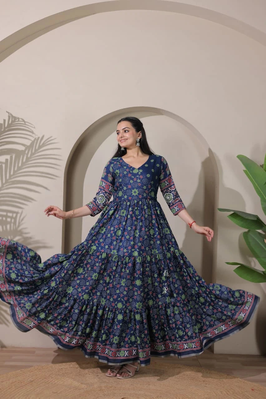 Woman in a blue floral dress standing in front of an archway with plants.