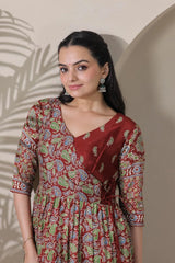 Woman wearing a patterned dress standing against a neutral wall.