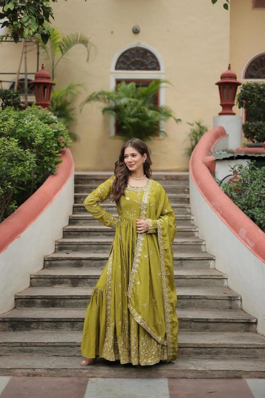 Woman in a green traditional outfit standing on a staircase with a building and plants in the background
