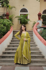 Woman in a green traditional outfit standing on a staircase with a building and plants in the background