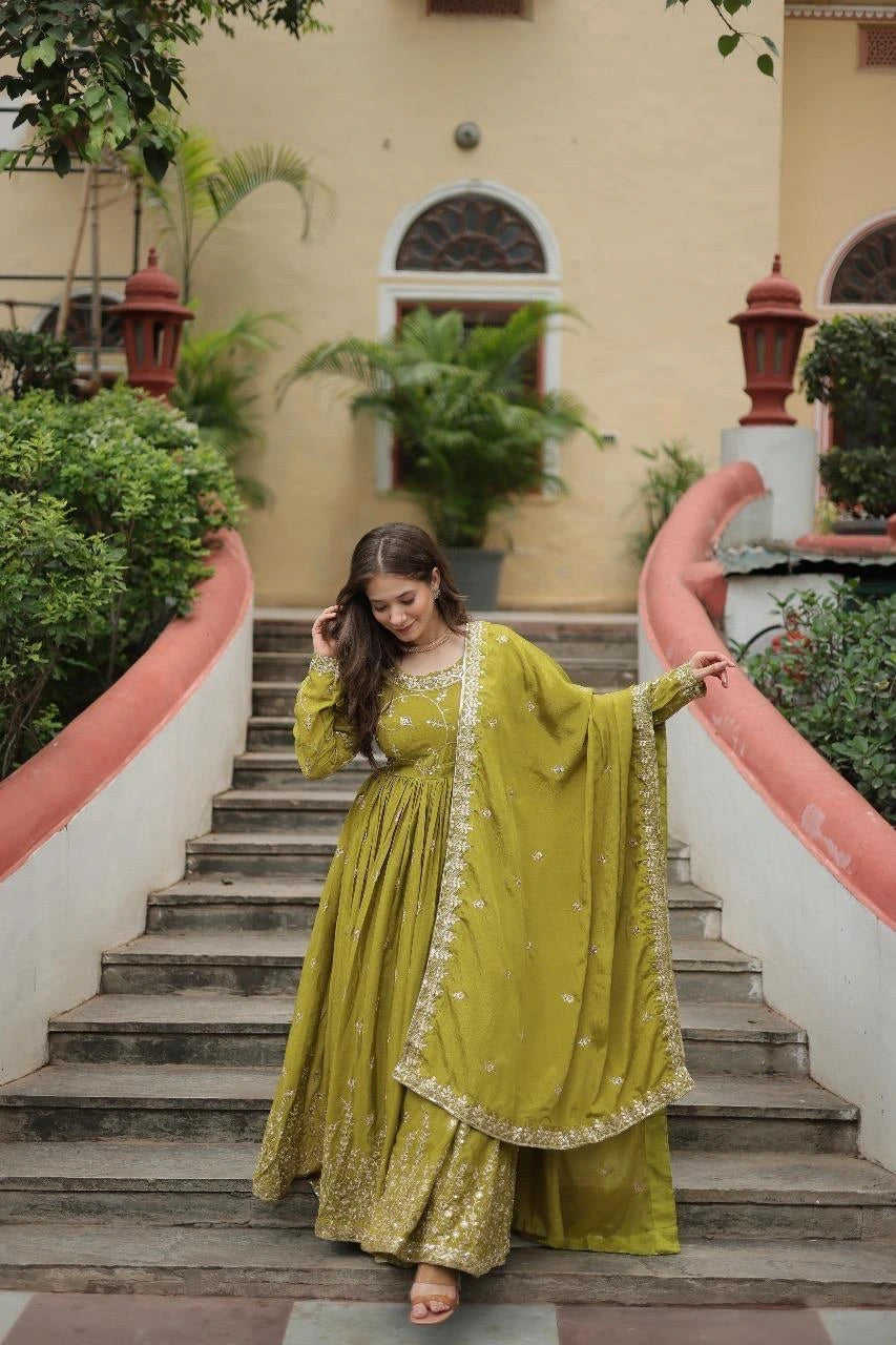 Woman in a green traditional outfit standing on a staircase with a building and plants in the background