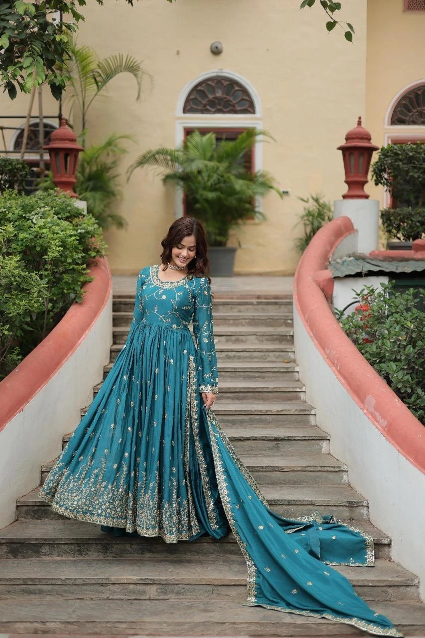 Woman in a blue traditional dress standing on a staircase with greenery and a building in the background