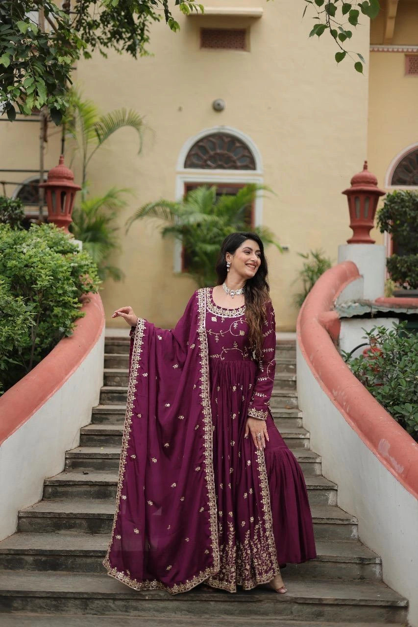 Woman in a purple traditional outfit standing on a staircase with greenery and a building in the background