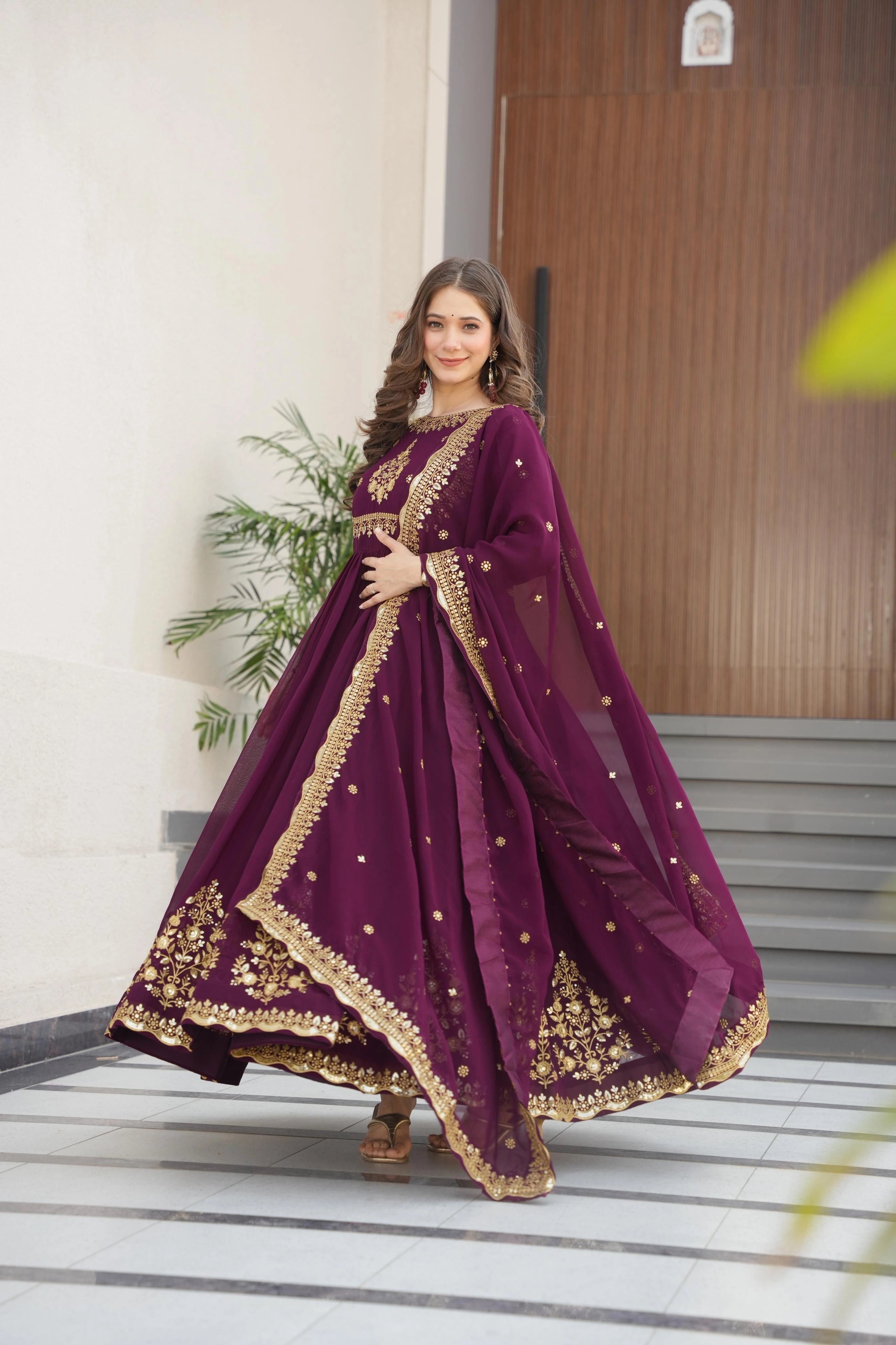 Woman in a purple traditional outfit with gold embroidery standing indoors.