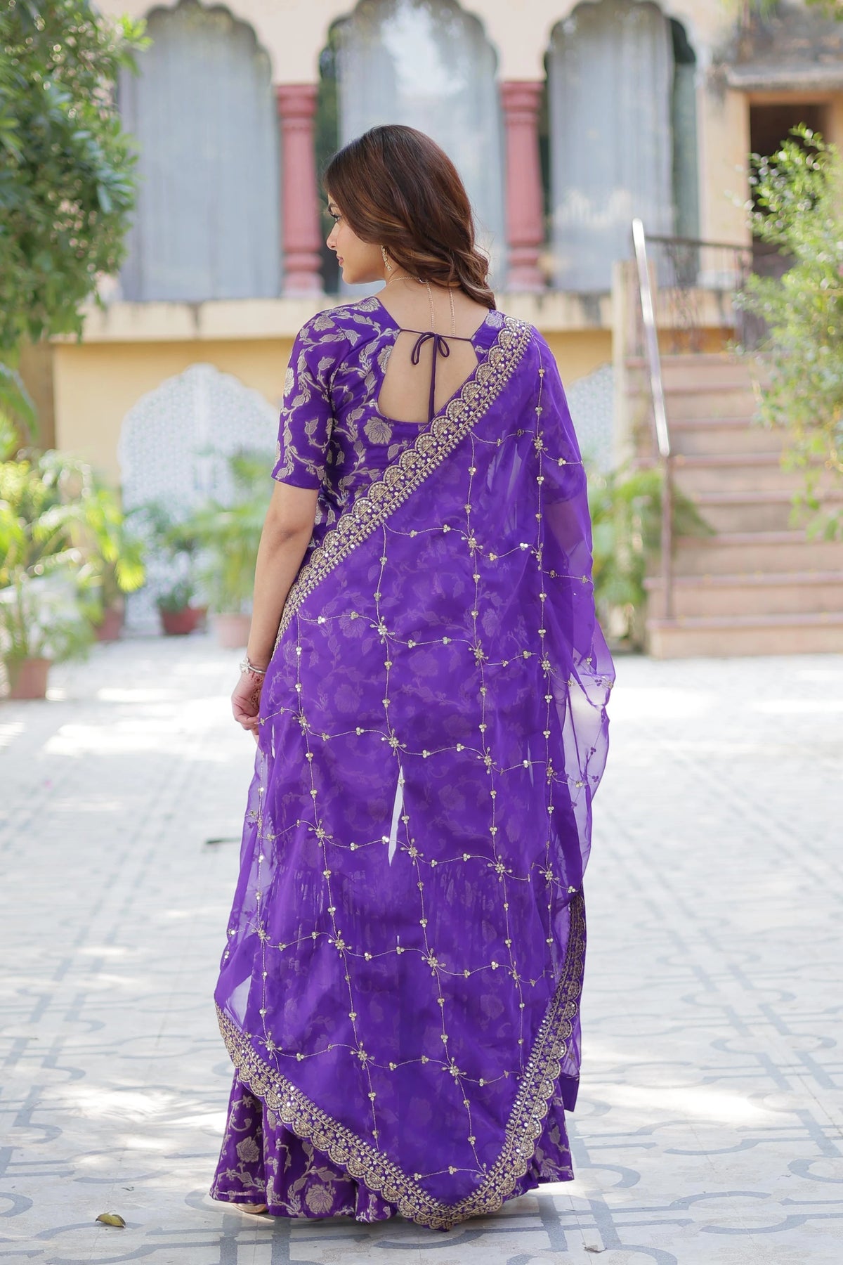Woman wearing a purple saree with a traditional design, standing outdoors.