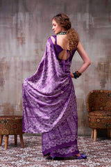 Woman in a purple saree with a textured wall and patterned chair in the background