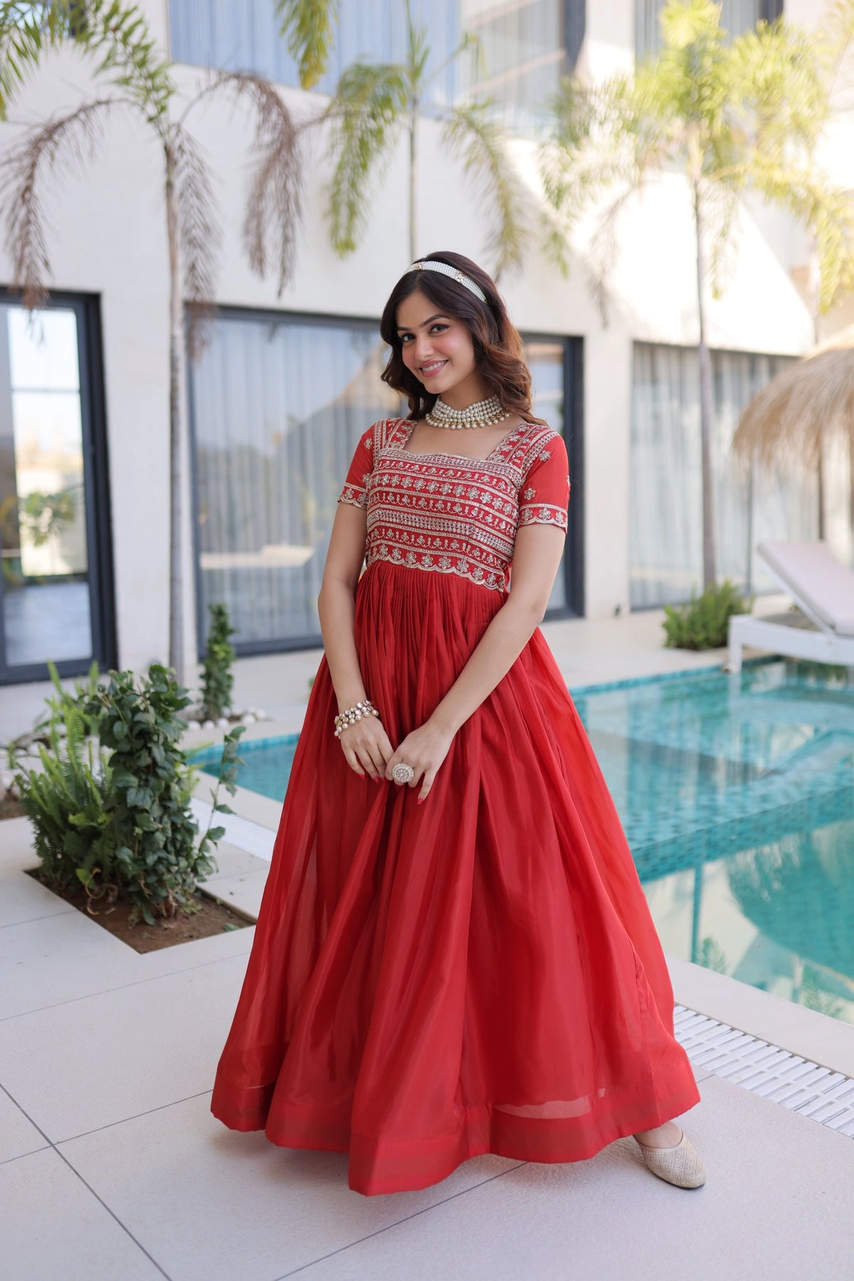 Woman in a red dress standing by a pool with a modern building in the background