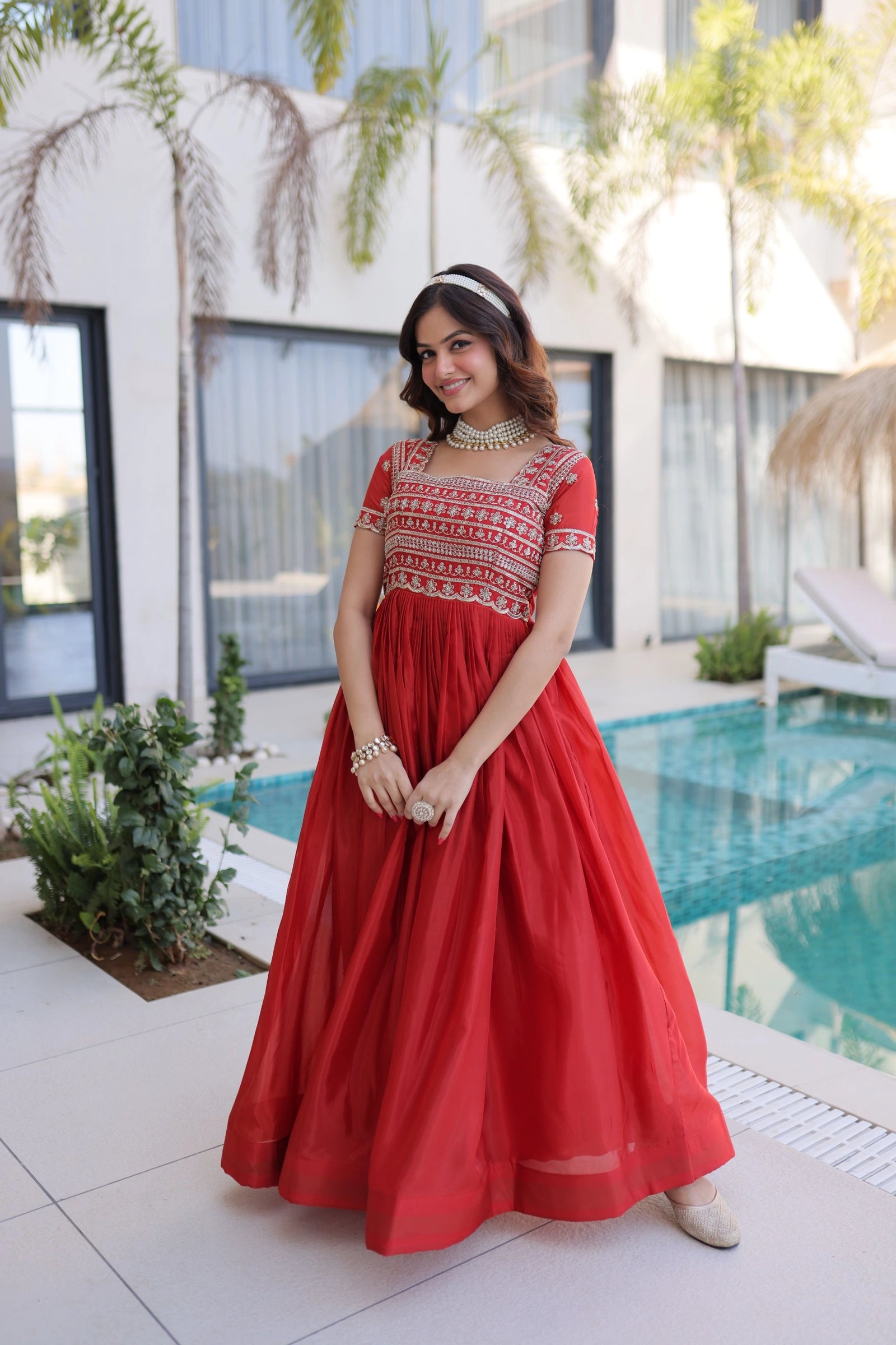 Woman in a red dress standing by a pool with a modern building in the background