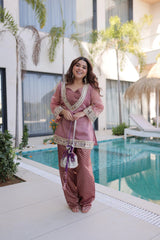 Woman in a pink traditional outfit standing by a poolside with plants and a building in the background.