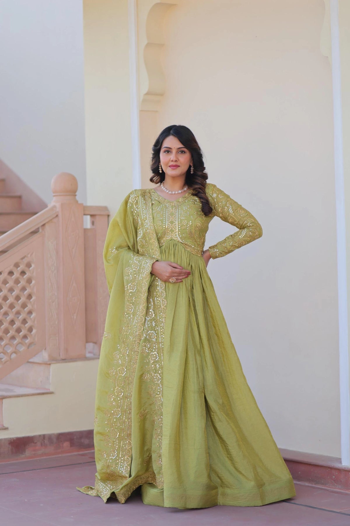 Woman in a green traditional outfit standing in front of a staircase.