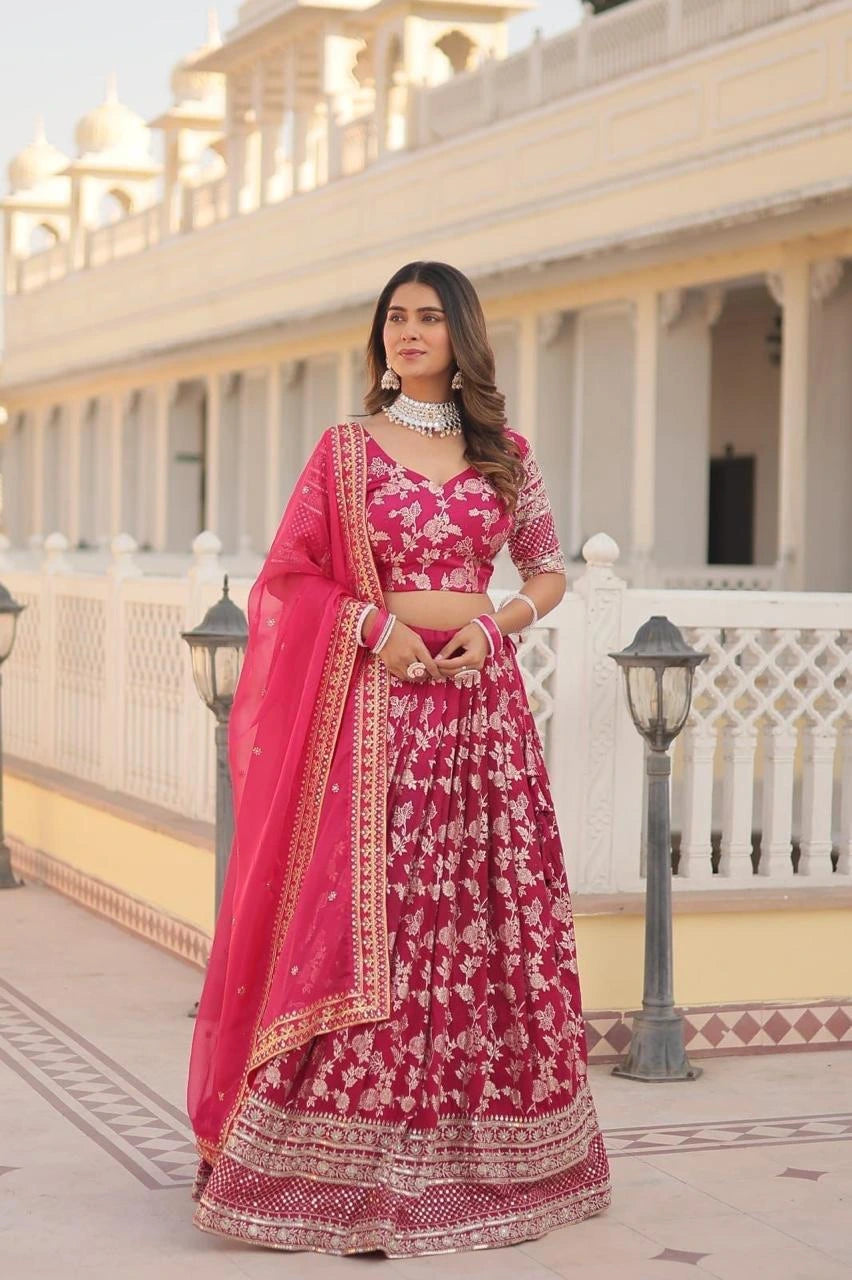Woman in a traditional pink and red embroidered outfit standing in front of a building with white columns.
