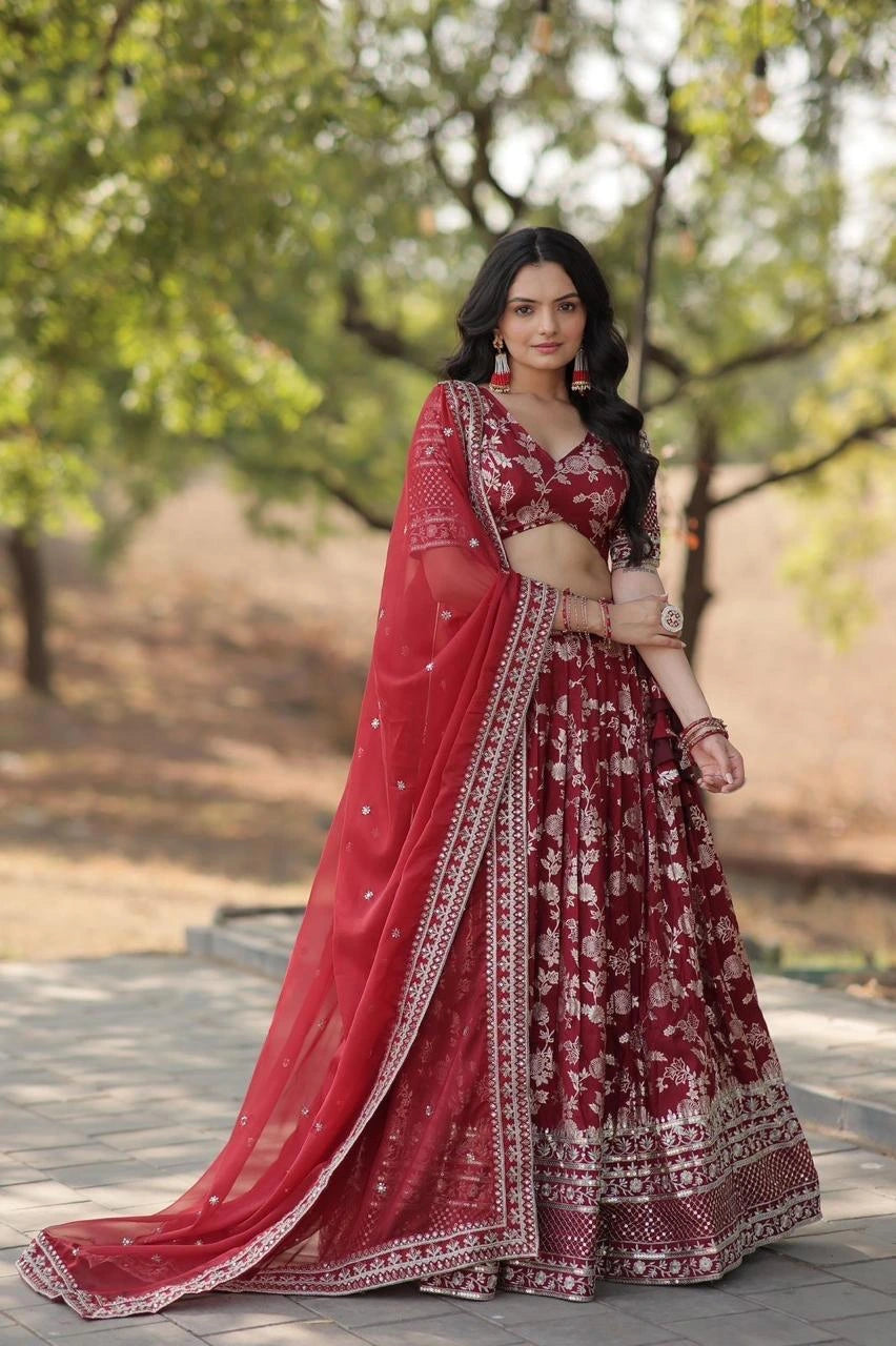 Woman in a red and maroon traditional outfit standing outdoors with trees in the background