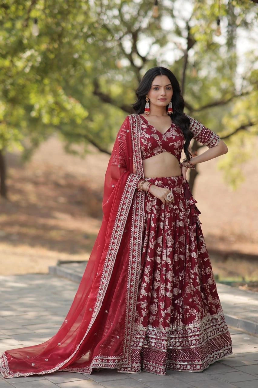 Woman in a red and white embroidered traditional outfit standing outdoors with greenery in the background
