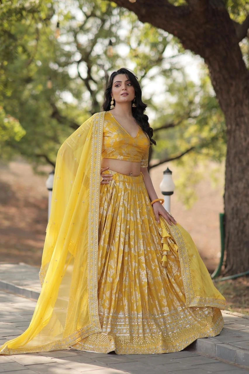 Woman in a yellow traditional outfit standing outdoors with trees in the background