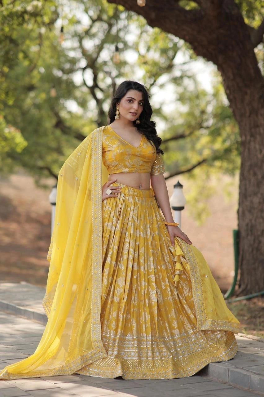 Woman in a yellow traditional outfit standing outdoors with trees in the background