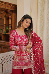 Woman in a red and pink embroidered traditional outfit standing indoors.