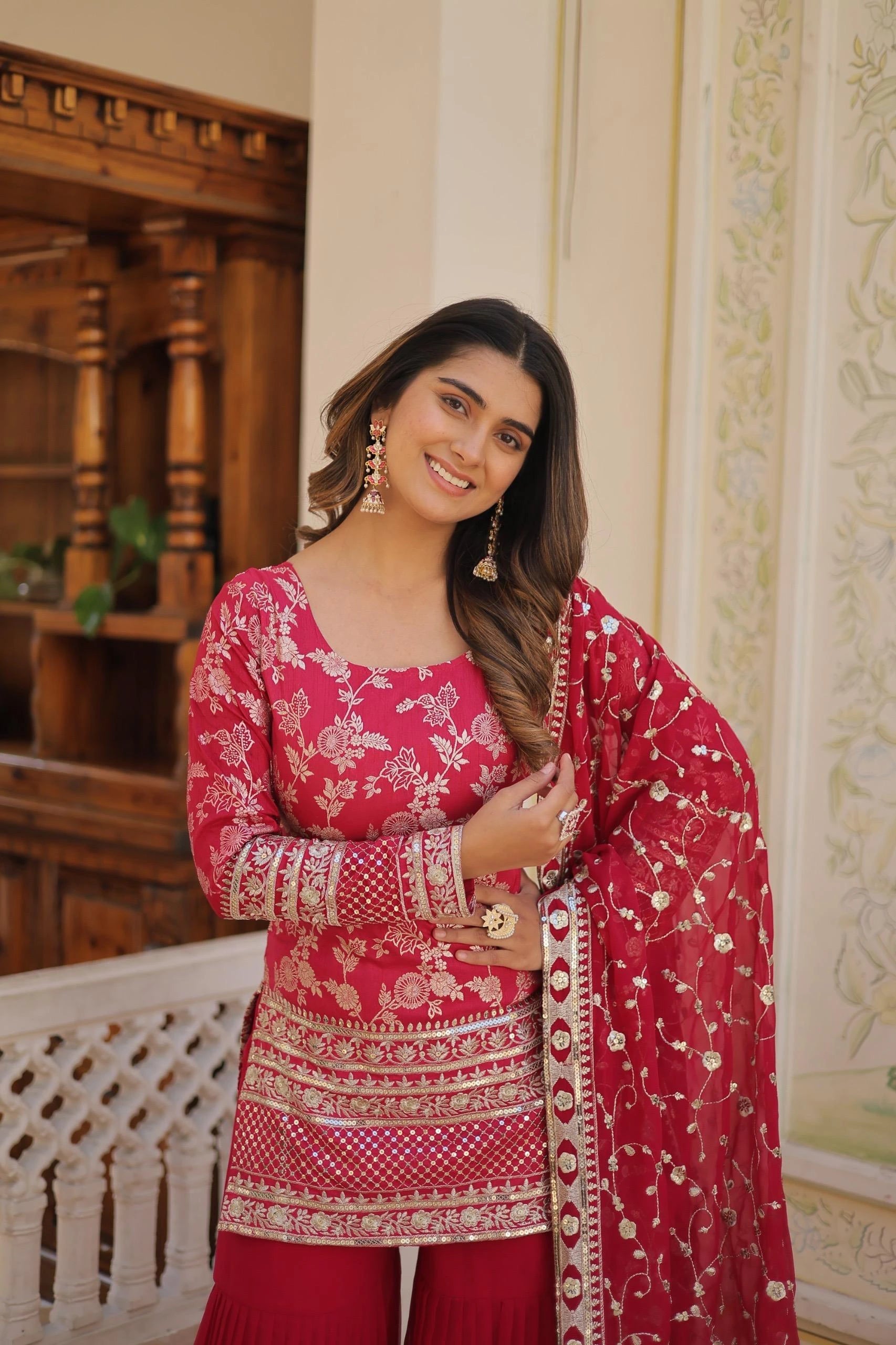 Woman wearing a red and pink traditional outfit with a matching dupatta indoors.
