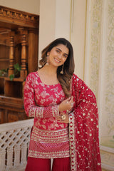 Woman wearing a red and pink traditional outfit with a matching dupatta indoors.