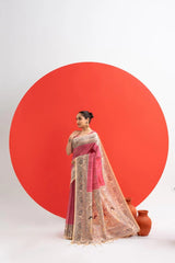Woman in a pink saree with intricate patterns standing against a white background with a large red circle.
