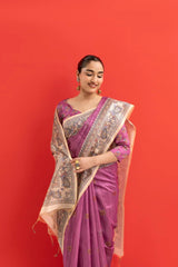 Woman wearing a pink saree with a gold border against a red background