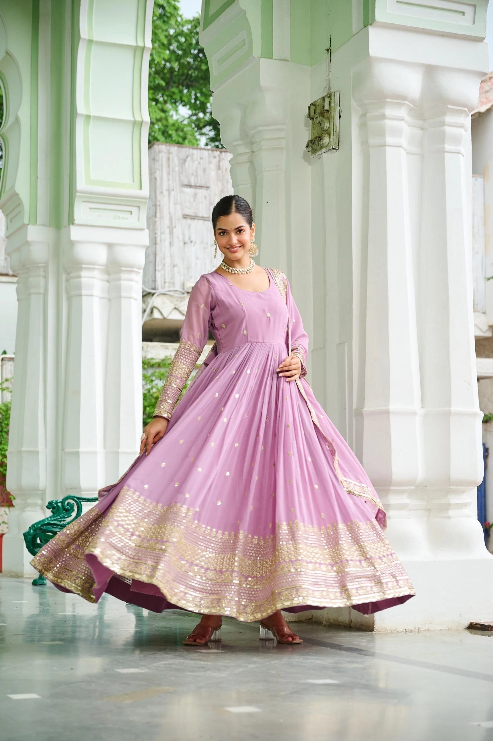 Woman in a pink and gold traditional outfit standing in a temple-like setting.