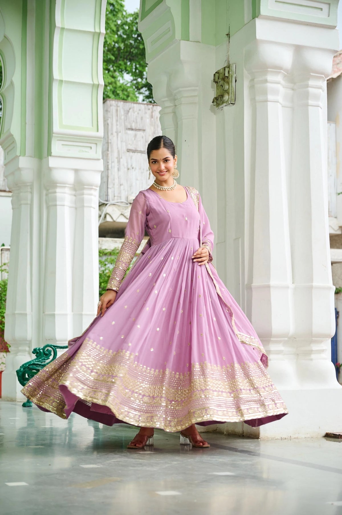 Woman in a pink and gold traditional outfit standing in a temple-like setting.