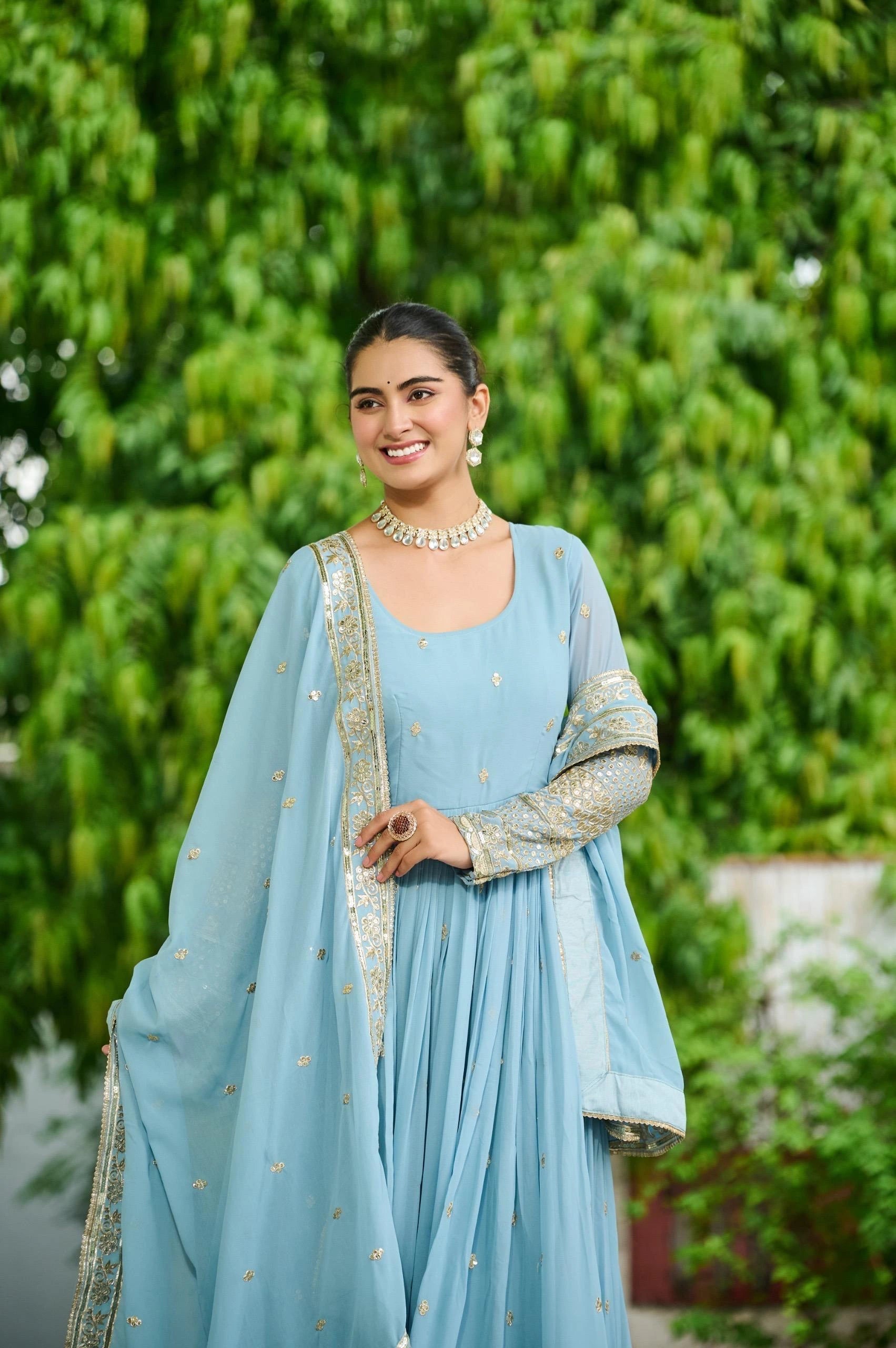 Woman in a light blue traditional outfit with a green leafy background