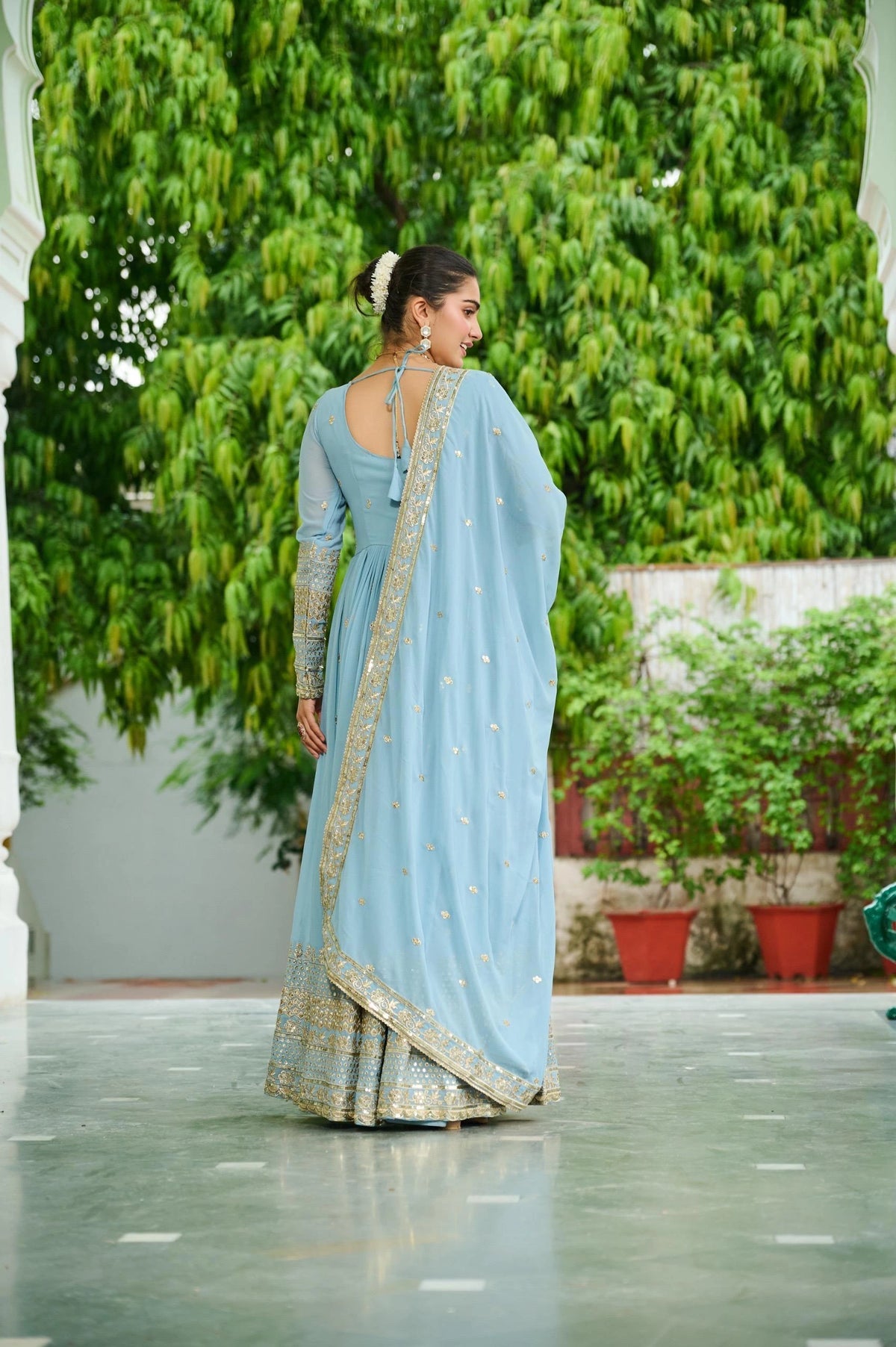 Woman in a light blue saree with a green garden background