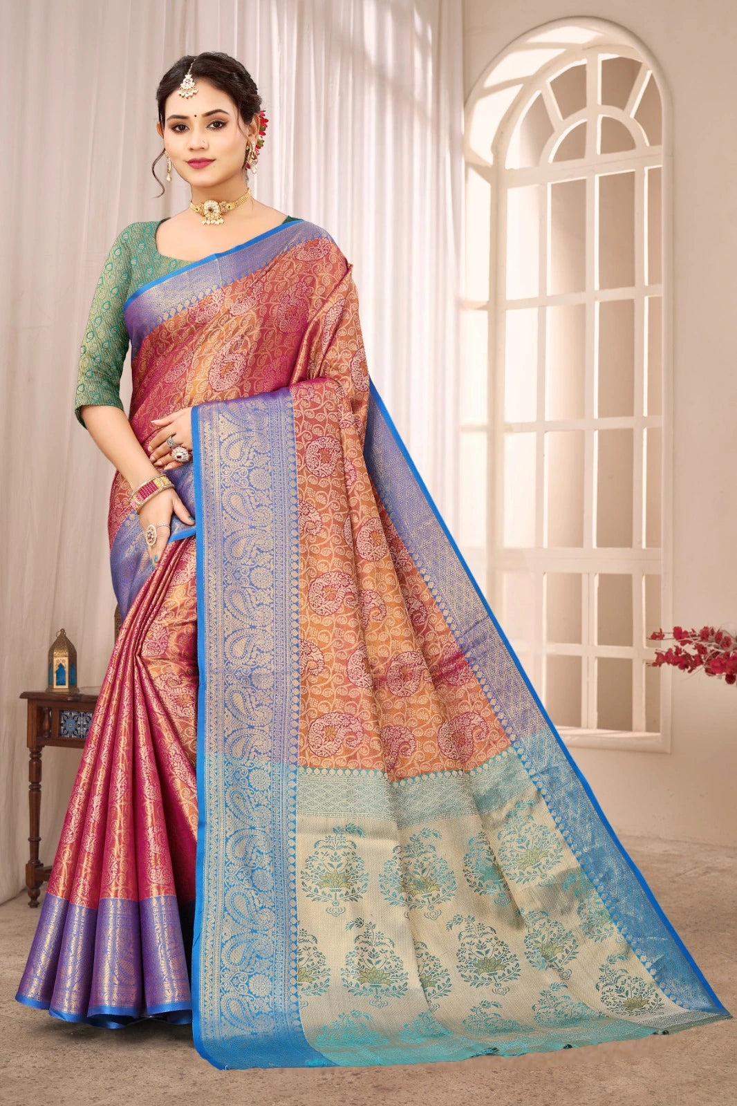 Woman wearing a colorful saree in a well-lit room with curtains and a window.