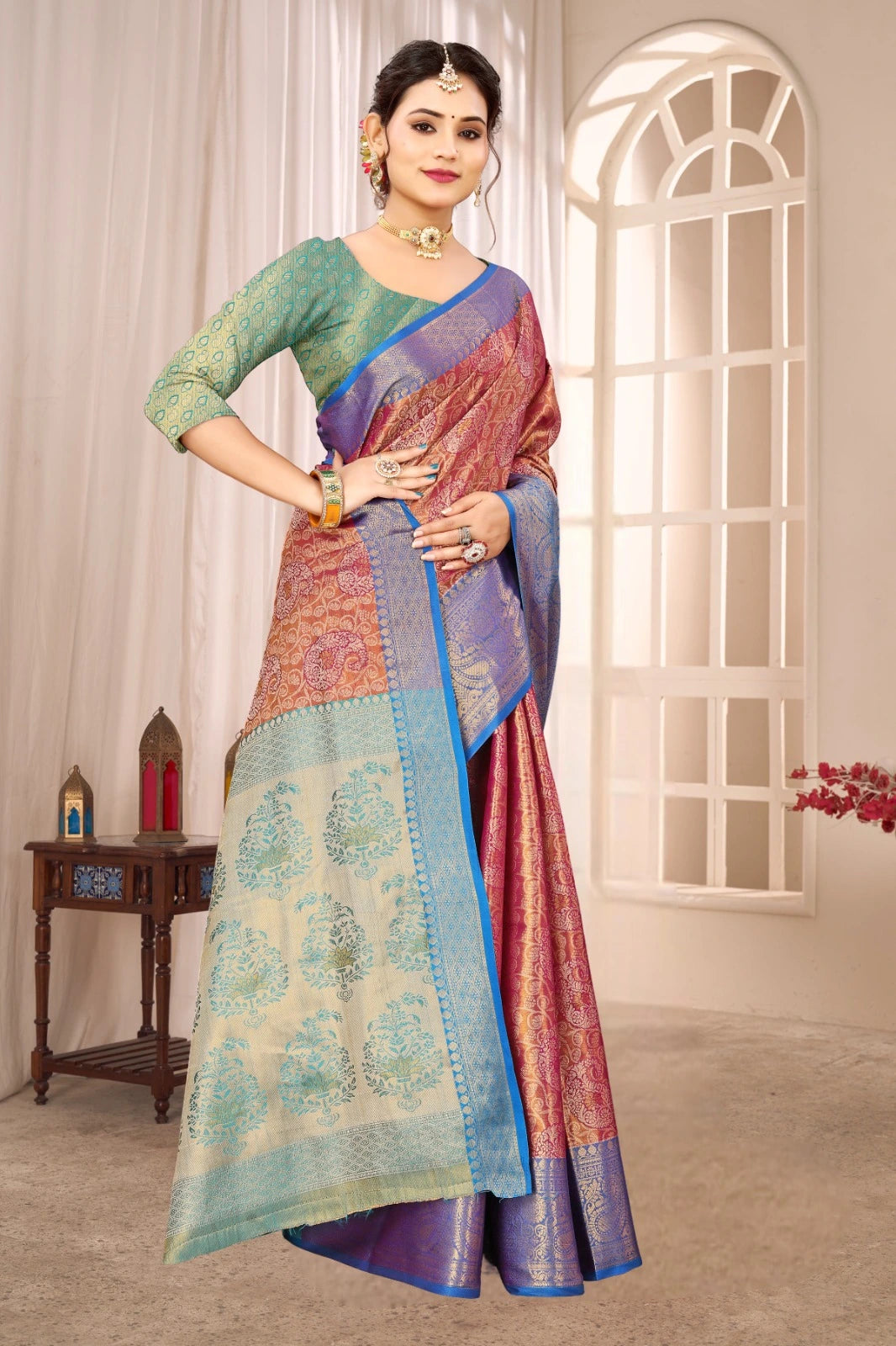 Woman wearing a colorful saree in a well-lit room with a window and small table.