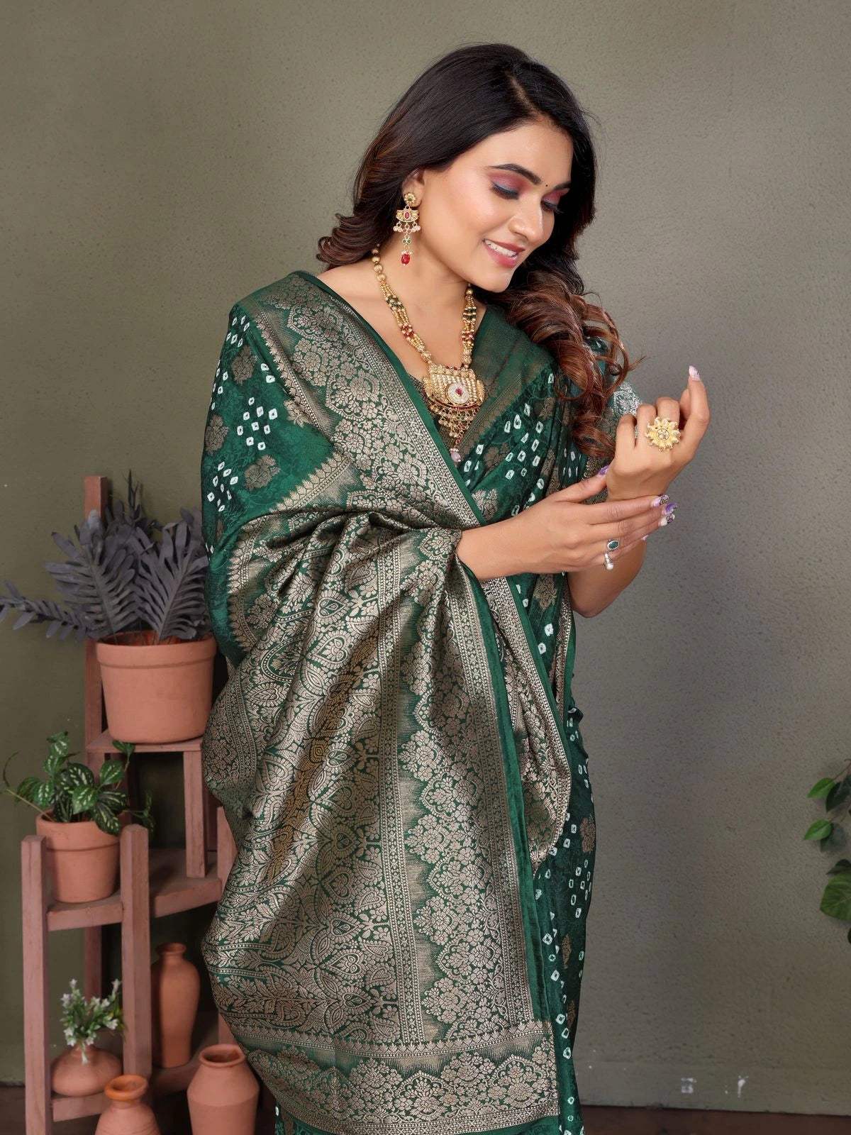 Woman in a green and gray patterned saree holding jewelry against a neutral background