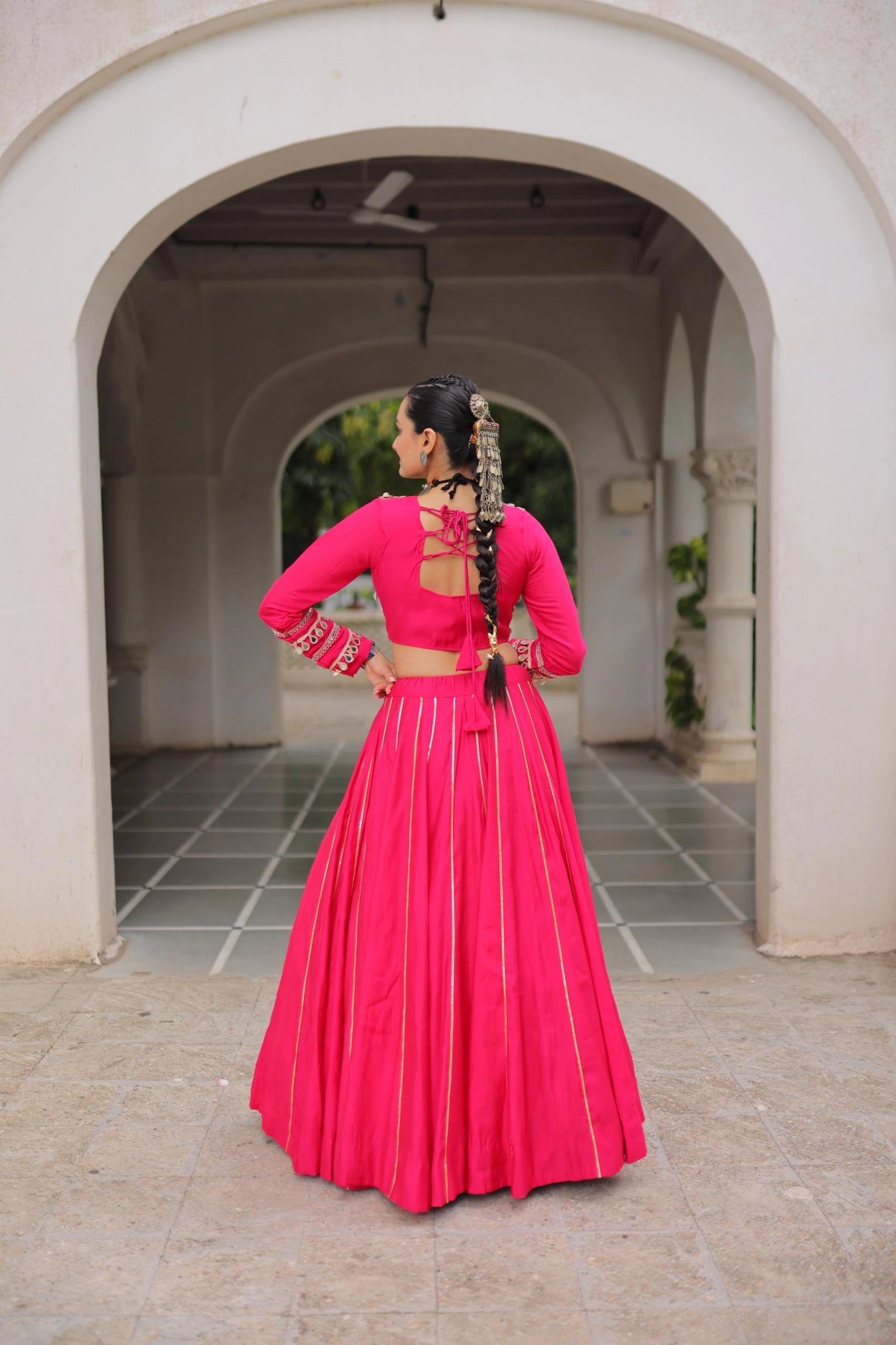 Person wearing a bright pink traditional outfit with a backless top and long skirt, standing in an archway.