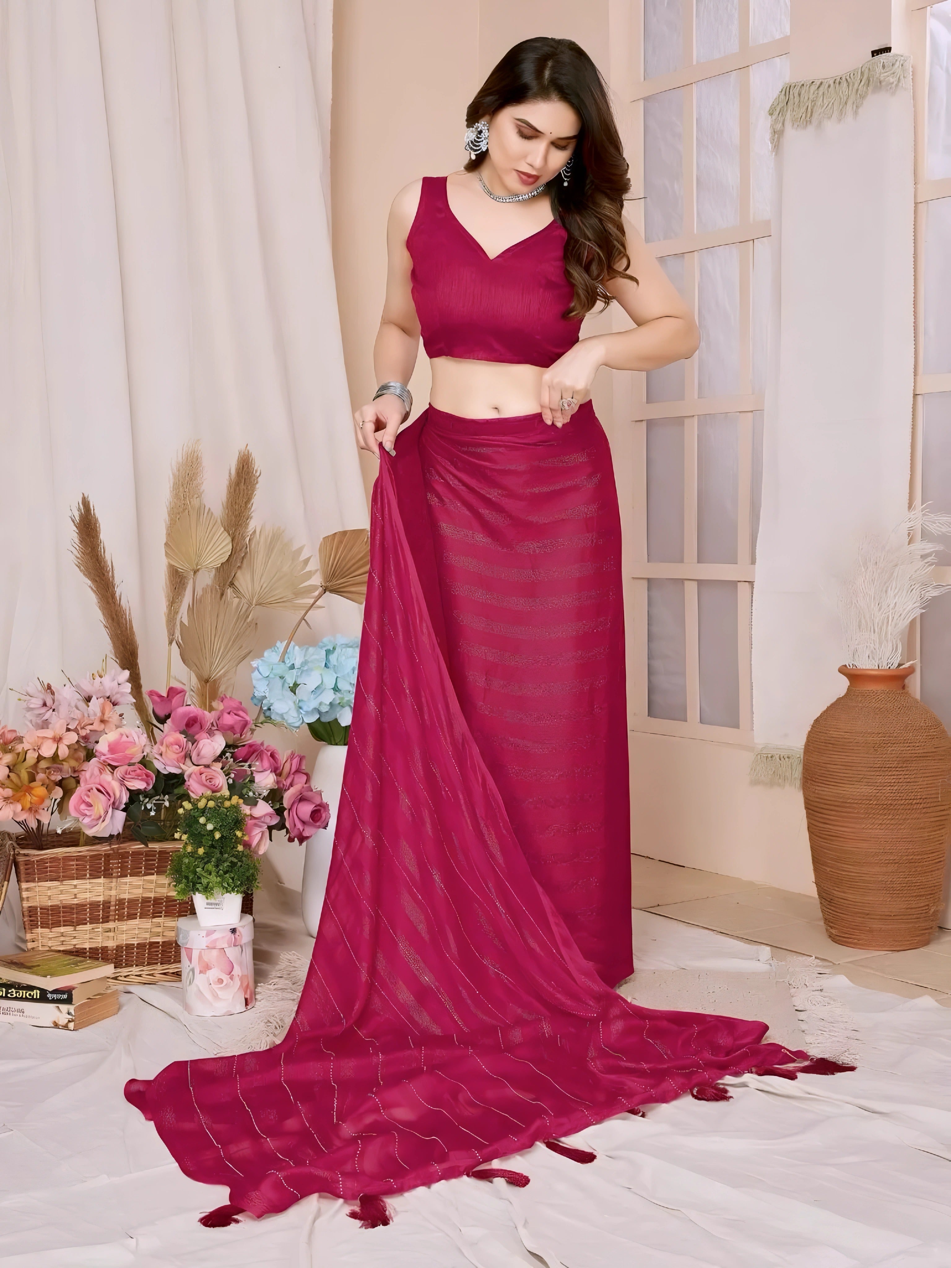 A woman models a vibrant Dark Pink Rimzim Silk Saree. The sheer fabric features prominent vertical stripes of fine metallic (silver) threadwork and subtle dot embellishments. She wears a matching sleeveless pink V-neck blouse and accessorizes with chunky oxidized silver jewelry, including a layered necklace and thick bangles.