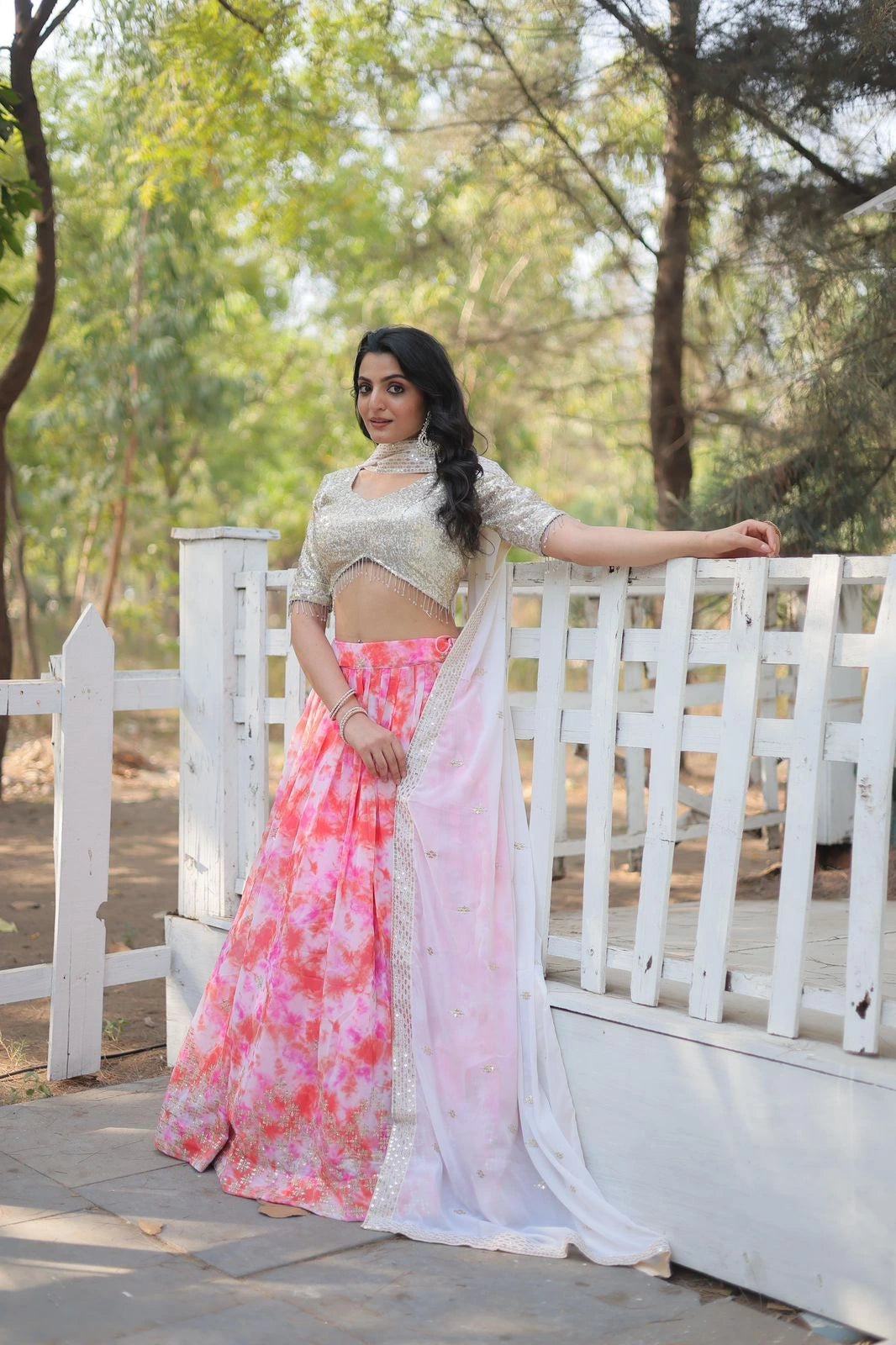 Woman in a floral saree standing on a wooden bridge with greenery in the background
