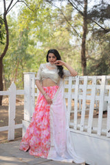 Woman in a pink and white saree standing on a wooden bridge with greenery in the background